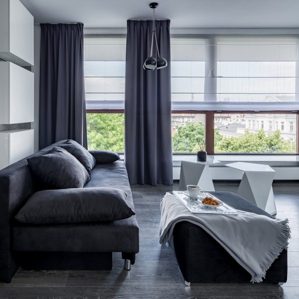 Large gray couch with ottoman and food tray, long gray curtains to match and white shades.